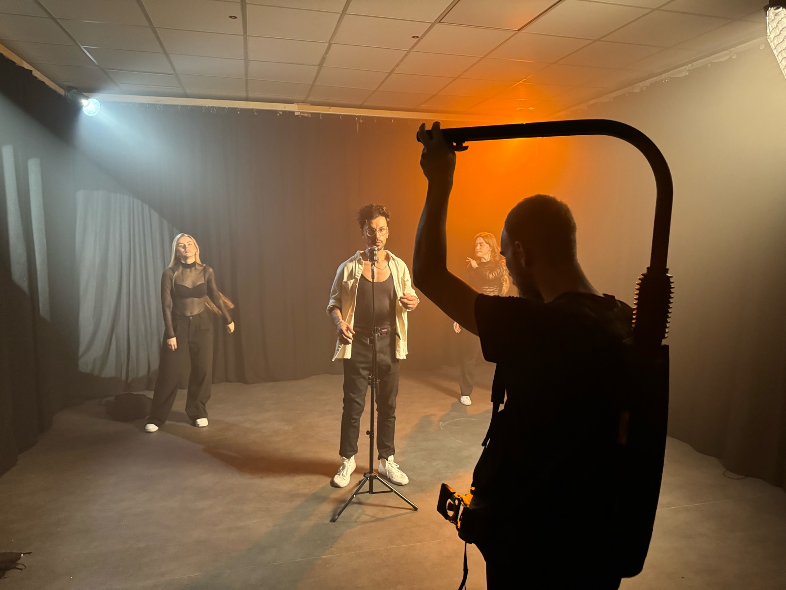 Steadicam-Operator als Silhouette vor Sänger und Tänzerinnen im Nebel mit Blau-Orange-Licht.