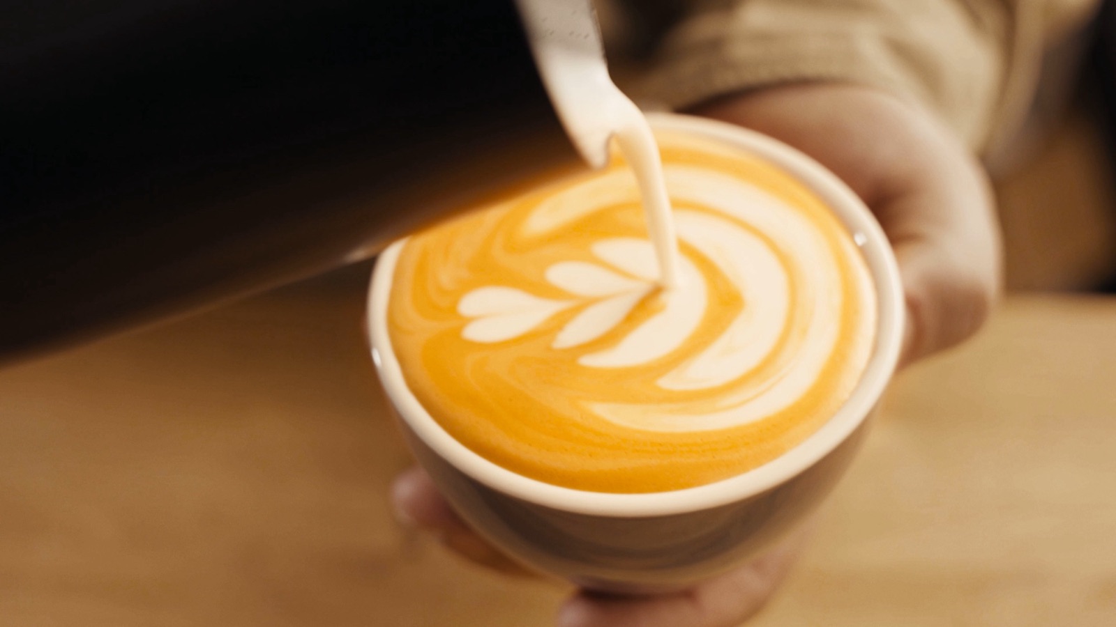 Latte Art wird in eine Tasse gegossen, warmes Licht (Bärista).